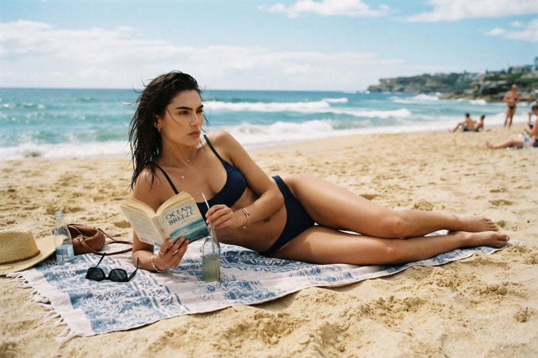 A cold-faced female model in a black bikini is lying on a towel reading a book